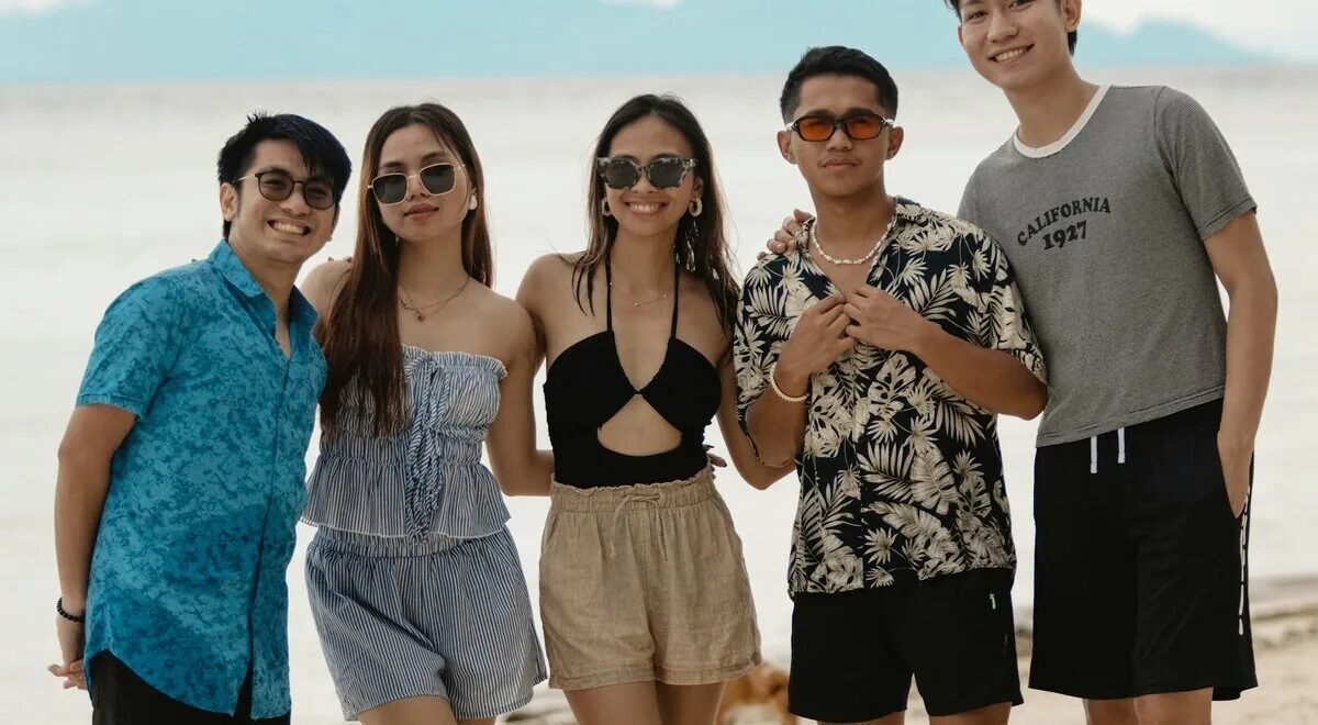Grupo de jóvenes filipinos sonriendo en una playa tropical con montañas de fondo